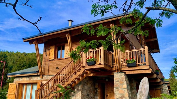 Una cabaña de madera con base de piedra, balcones de madera y una escalera que lleva a la entrada.
