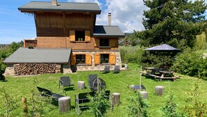 Una casa de madera con cimientos, pared y chimenea de piedra. Hay sillas exteriores y una mesa de picnic.