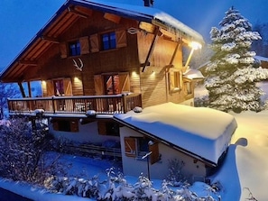 Een houten chalet met balkon, een besneeuwde omgeving en een zichtbare schoorsteen.