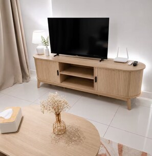 Un salon moderne avec un téléviseur à écran plat posé sur un meuble en bois, une lampe blanche et une petite plante.