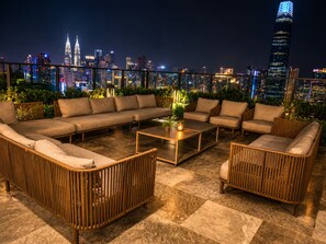 Un salon sur le toit offrant une vue panoramique sur la ville, avec un ensemble de canapés, une table basse et des meubles en osier.