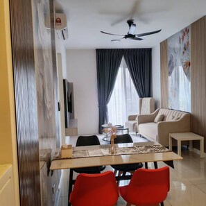 Ein modernes Wohnzimmer mit einer Couch, einem Esstisch mit Stühlen, einem Deckenventilator und einem großen Fenster mit Vorhängen.