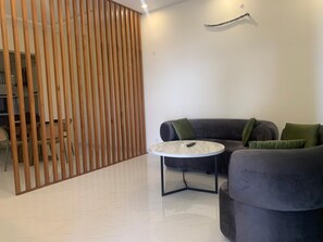 Een moderne woonkamer met een hoekbank, een ronde salontafel en een houten scheidingswand.