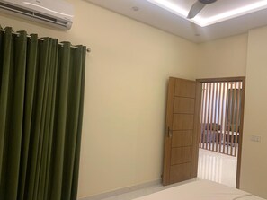 A room with a bed, a wooden wardrobe, a green curtain, and an air conditioning unit. - Perfect 1-bedroom apartment with AC in soothing Lahore (Lahore)
