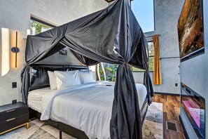 A modern bedroom with a canopy bed, a bedside table, and a view of a natural landscape. - Romantic Luxe Oasis•Private Pool•Mtn Views•Theater (Pigeon Forge)