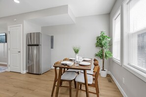 Eine moderne Küche mit einem eingebauten Edelstahlkühlschrank, einem Esstisch gedeckt mit weißen Tellern und Schüsseln, und einer Topfpflanze.