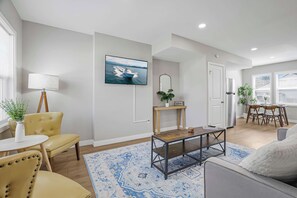 A modern living room with a sofa, a coffee table, a TV, and a dining area with chairs and a table. - Olde Towne East Townhouse | Minutes to Downtown (Columbus)