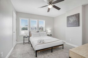 A bedroom with a bed, a ceiling fan, a nightstand with a lamp, and a window with blinds. - Olde Towne East Townhouse | Minutes to Downtown (Columbus)