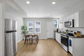 A modern kitchen with stainless steel appliances, a dining area with a table and chairs, and a view of the outside through the windows. - Olde Towne East Townhouse | Minutes to Downtown (Columbus)