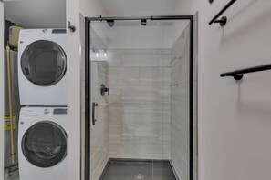 Ein Waschraum mit zwei Waschmaschinen mit Frontlader, einem gläsernen Duschbereich und einer gefliesten Wand.