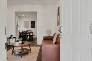 Uma sala de estar com um sofá de couro marrom, uma mesa de centro de madeira e uma área de jantar com mesa e cadeiras.