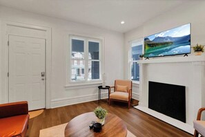 A living room with a fireplace, a television mounted above it, and a window with blinds. - Olde Towne East 4BR Townhome Near East Market (Columbus)
