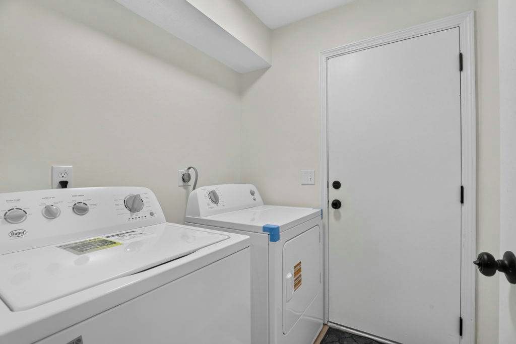 A laundry room with a front-loading washer and dryer, a door with a black handle, and a white wall.