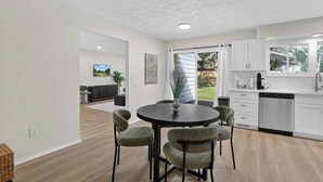 A modern kitchen with white cabinets, a dishwasher, and a dining area with a round table and chairs. - Cozy Reynoldsburg Home with Fireplace & Garage (Reynoldsburg)