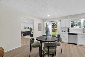 Een moderne keuken met witte kastjes, een vaatwasser en een eethoek met een ronde tafel en stoelen.