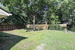 Un jardin à l’arrière de la maison, avec un arbre, une clôture en bois et un petit espace potager.