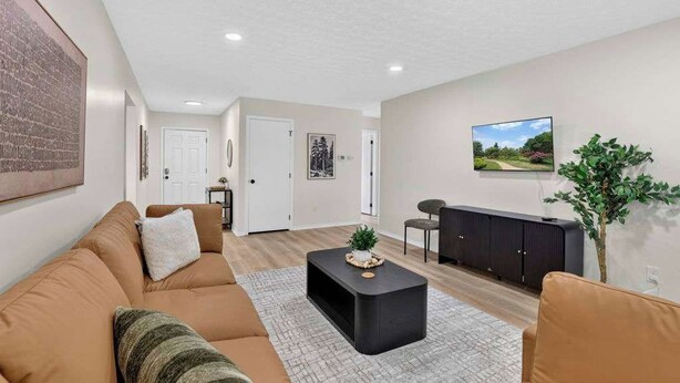 A living room with a sofa, coffee table, and a television. There is a door leading to another room. - Cozy Reynoldsburg Home with Fireplace & Garage (Reynoldsburg)