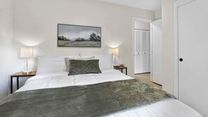 A bedroom with a bed, two bedside lamps, a painting on the wall, and a door leading to another room. - Cozy Reynoldsburg Home with Fireplace & Garage (Reynoldsburg)