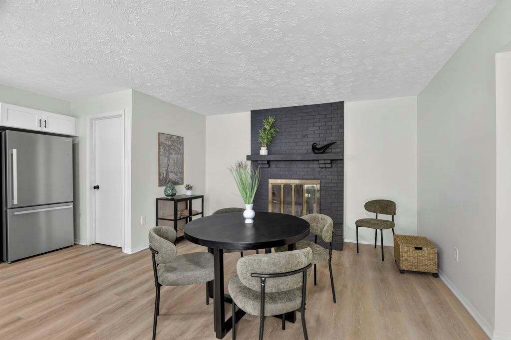 A modern kitchen with a built-in refrigerator, a dining area with a round table and chairs, and a dark brick fireplace.