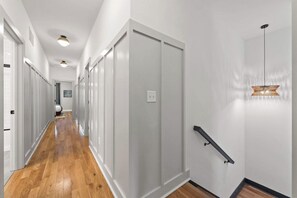 A hallway with wooden flooring, white walls, and a grey door. There is a light fixture on the ceiling and a black metal handrail on the wall. - FUNtastic Home! | 5 BR - Hot Tub + Game Room! (Columbus)
