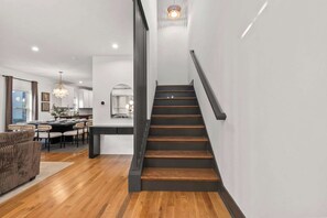 A modern interior with a staircase, wooden flooring, and a dining area with a kitchen in the background. - FUNtastic Home! | 5 BR - Hot Tub + Game Room! (Columbus)