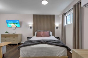 A modern bedroom with a bed, bedside tables, a TV, a wooden panel wall, and a window with curtains. - First-Floor New Columbus Studio Steps from Downtown (Columbus)