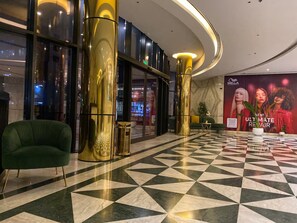 En lobby med et ternet gulv, en grøn lænestol og en stor guldfarvet søjle.