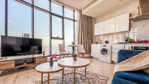 A modern living room with a large TV, two round tables, a sofa, and a view of the city through large windows. - Best for get away & Peaceful Haven by Flouri F282O (Seef)
