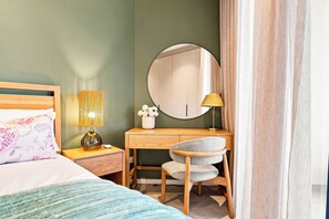 A bedroom with a bed, a desk with a chair, a mirror, and a lamp. - Luxe 2BR York | Ocean-View | AC | Balcony (Umhlanga)