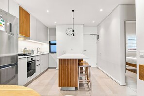 A modern kitchen with a stainless steel refrigerator, a built-in oven, and a wooden island with stools. - Luxe 2BR York | Ocean-View | AC | Balcony (Umhlanga)