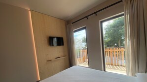 Une chambre d’hôtel avec un lit, un téléviseur fixé au mur, une porte coulissante donnant sur un balcon et un mur en bois.