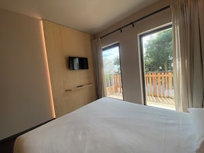 A hotel room with a bed, a mounted TV, a sliding door to a balcony, and a wooden wall. - Rifugio San Bernardo (Veneto)