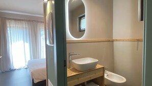 Een moderne hotelbadkamer met een grote, ovale spiegel, een wastafel op voet en een hygiëneschuiver.