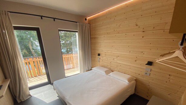 Een slaapkamer met een bed, houten wanden, een balkon en uitzicht op de omgeving.