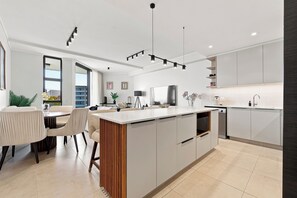 A modern kitchen with a central island, built-in appliances, and a dining area with a view. - Luxury 3 Bed Apartment |Balcony, Pool and Gym (Umhlanga)