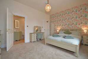 Ein Schlafzimmer mit einem Bett, Nachttischen, einem Schminktisch, einem Spiegel und einer Tür zu einem Badezimmer.