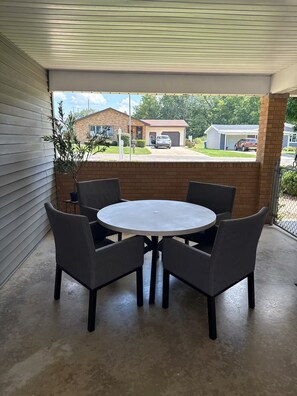 A covered patio area with a round table and four chairs, a potted plant, and a view of a residential street. - Welcome to Streator Hilltop - 3 bedroom home fully renovated and beautiful! (Streator)