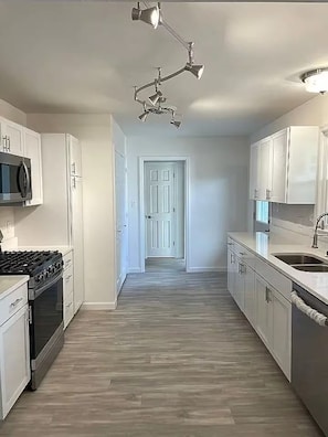 A modern kitchen with white cabinets, a stainless steel range hood, and a wooden floor. - Welcome to Streator Hilltop - 3 bedroom home fully renovated and beautiful! (Streator)