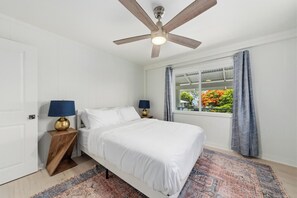 A bedroom with a bed, two bedside tables with lamps, a ceiling fan, a window with curtains, and a view of greenery outside. - Kahaluu Beach, 2-bed 2-bath, AC, steps to beach (Kailua-Kona)