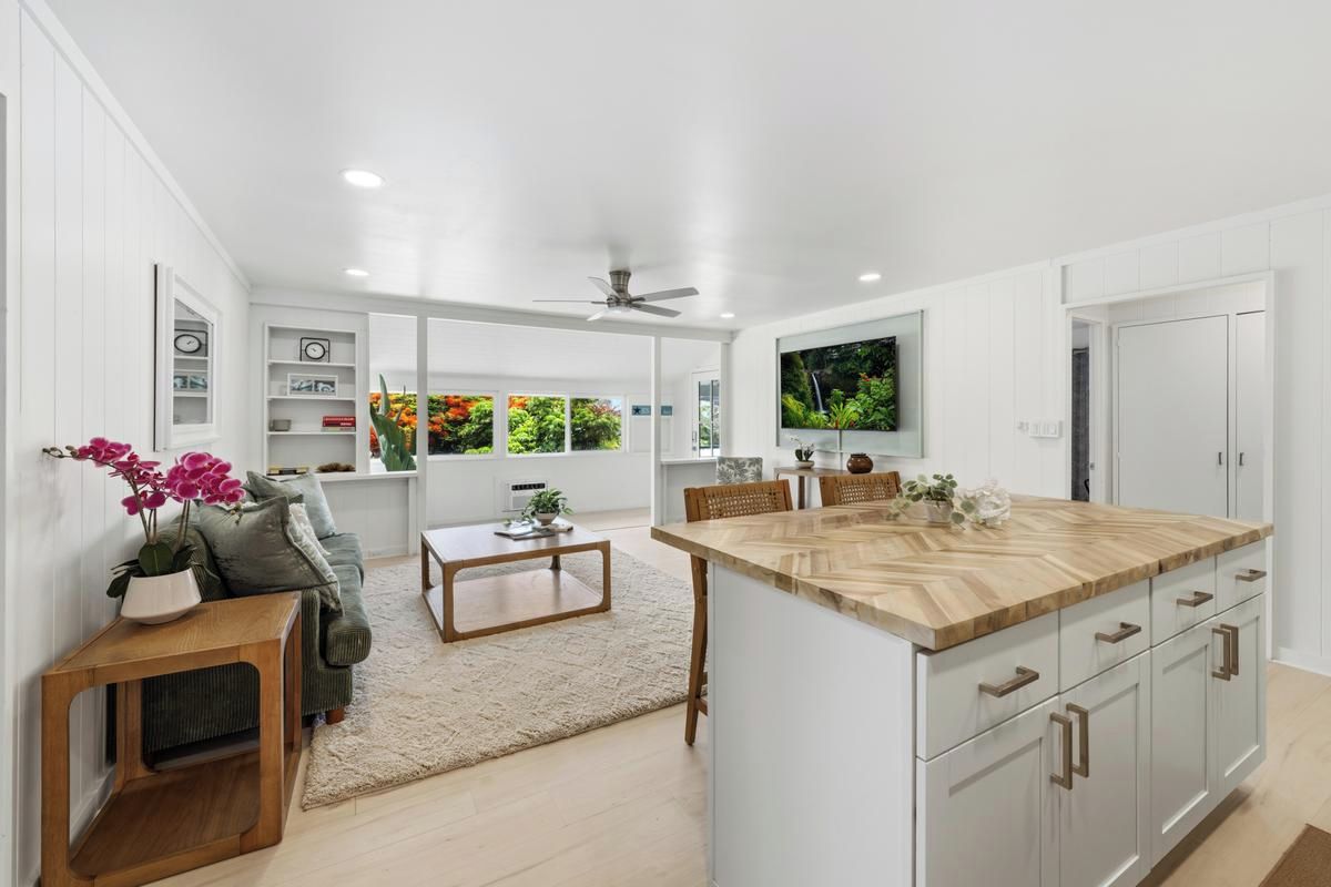 A modern kitchen with a central island, white cabinetry, and a dining area with a sofa and coffee table.