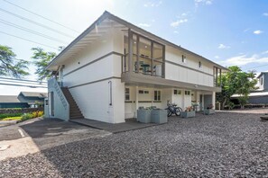 Un edificio a due piani con un balcone, una scala e un vialetto sterrato.