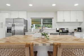 Una cucina moderna con mobili bianchi, un frigorifero in acciaio inossidabile, un tavolo da pranzo in legno e vista sull'esterno.