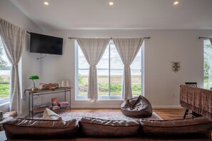 A living room with a leather sofa, a bean bag, a flat-screen TV, and a view of the outdoors. - Lakefront Champlain Duplex , King Bed & Bunk Bed w/ Kayaks, Pool & Fire Pit (Champlain)