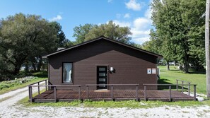 A small, single-story wooden cabin with a front door, a small porch, and a window. - Lakefront Champlain Duplex , King Bed & Bunk Bed w/ Kayaks, Pool & Fire Pit (Champlain)