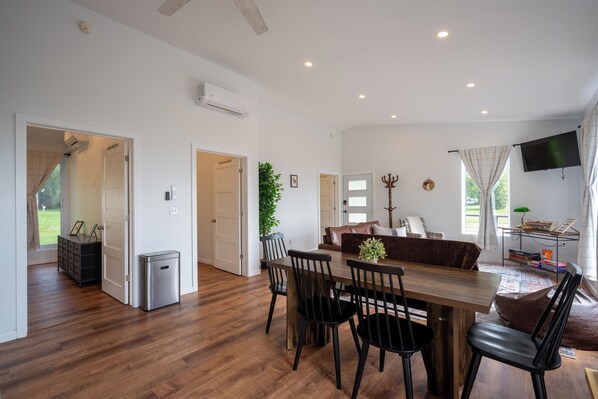 A spacious living area with a wooden dining table, chairs, a sofa, and a television. - Lakefront Champlain Duplex , King Bed & Bunk Bed w/ Kayaks, Pool & Fire Pit (Champlain)