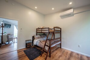 A bedroom with a bunk bed, a small bedside table, a nightstand, a floor lamp, a TV, and an air conditioning unit. - Lakefront Champlain Duplex , King Bed & Bunk Bed w/ Kayaks, Pool & Fire Pit (Champlain)