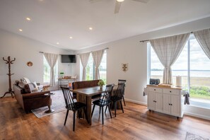 A spacious living area with a dining table, chairs, a sofa, and a TV mounted on the wall. - Lakefront Champlain Duplex , King Bed & Bunk Bed w/ Kayaks, Pool & Fire Pit (Champlain)