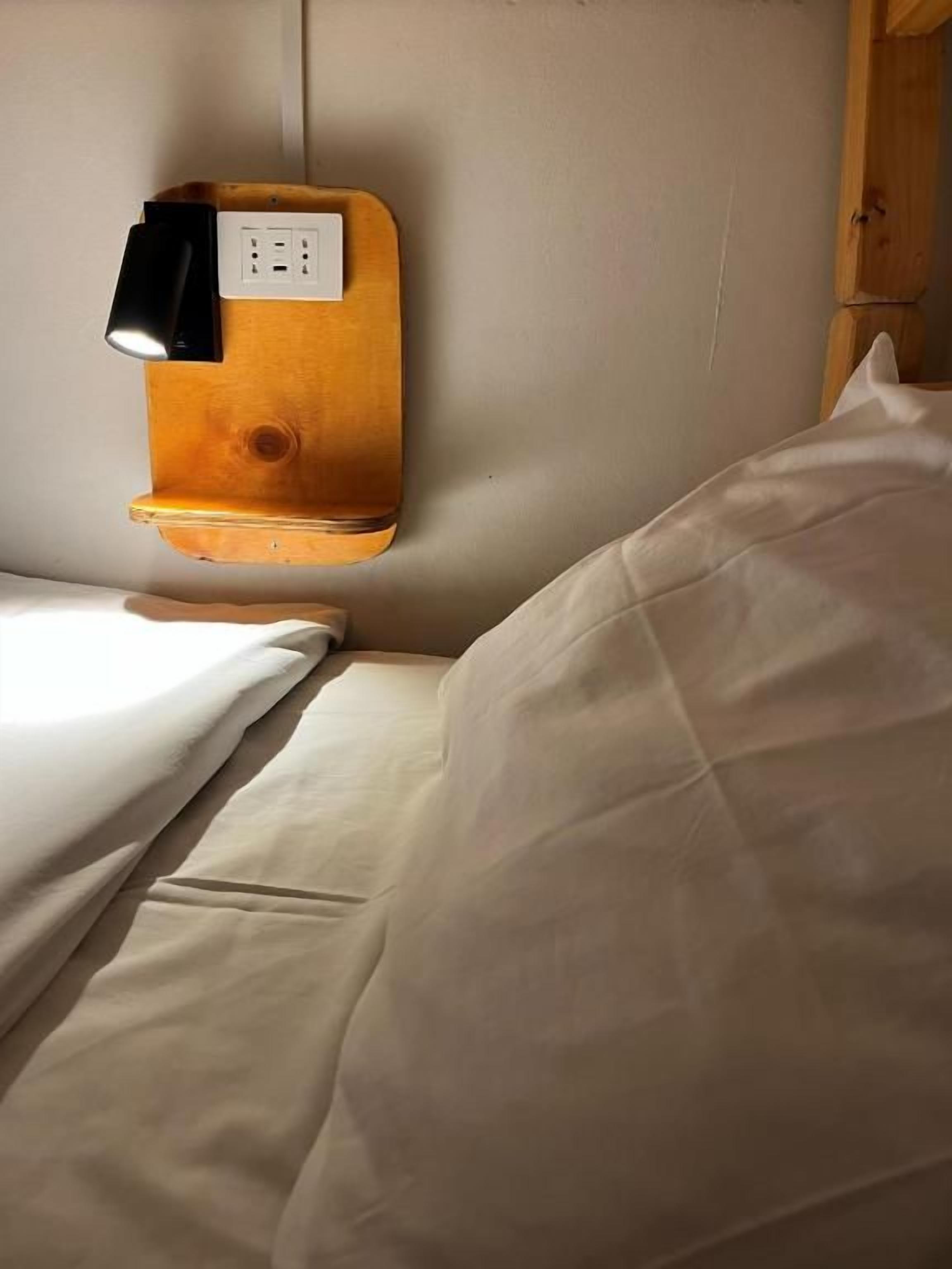 Una cama con cabecera de madera, una lámpara de noche y un enchufe.