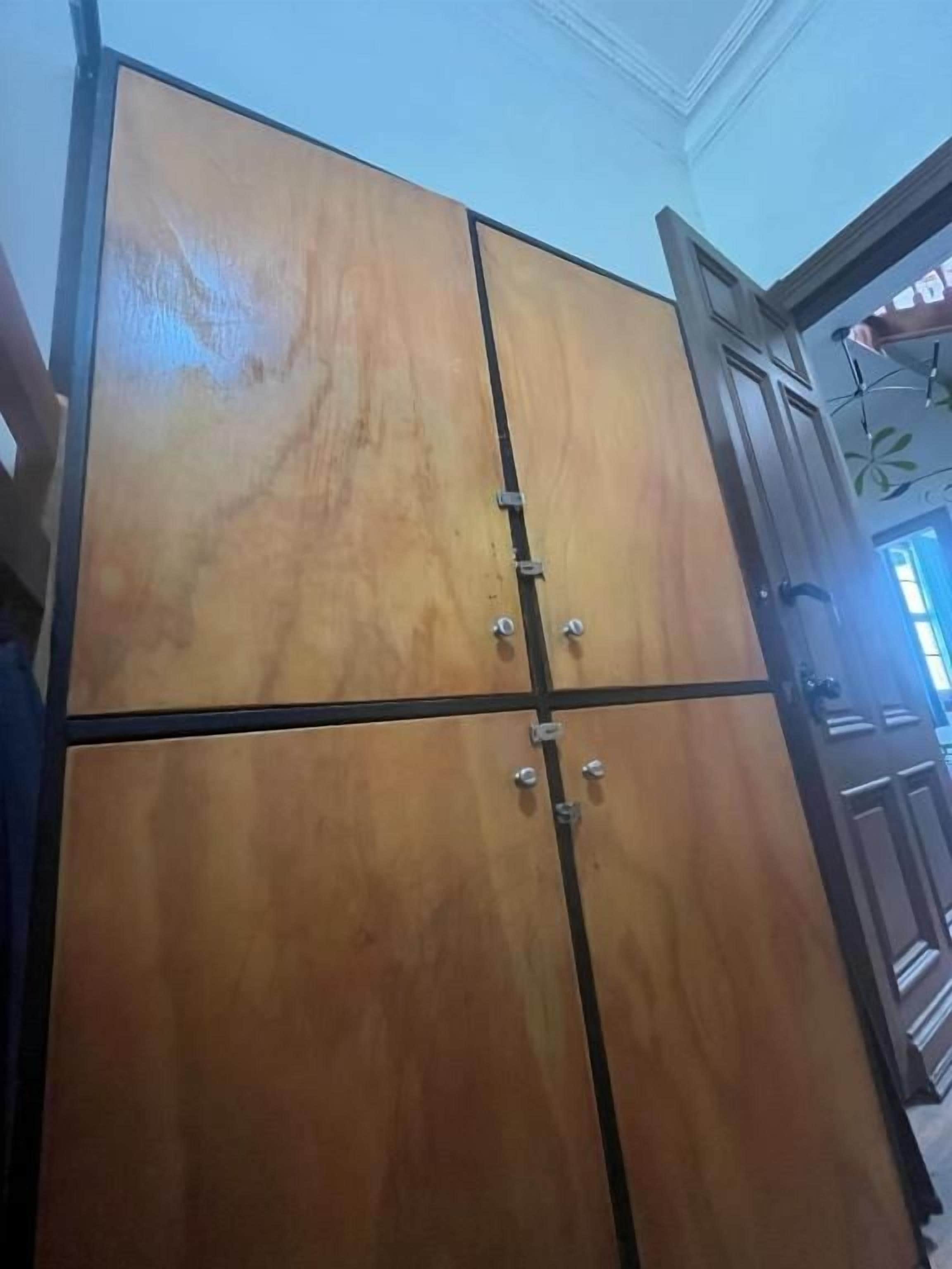 Un armario de madera con puerta espejada, un tirador y un pestillo metálico.