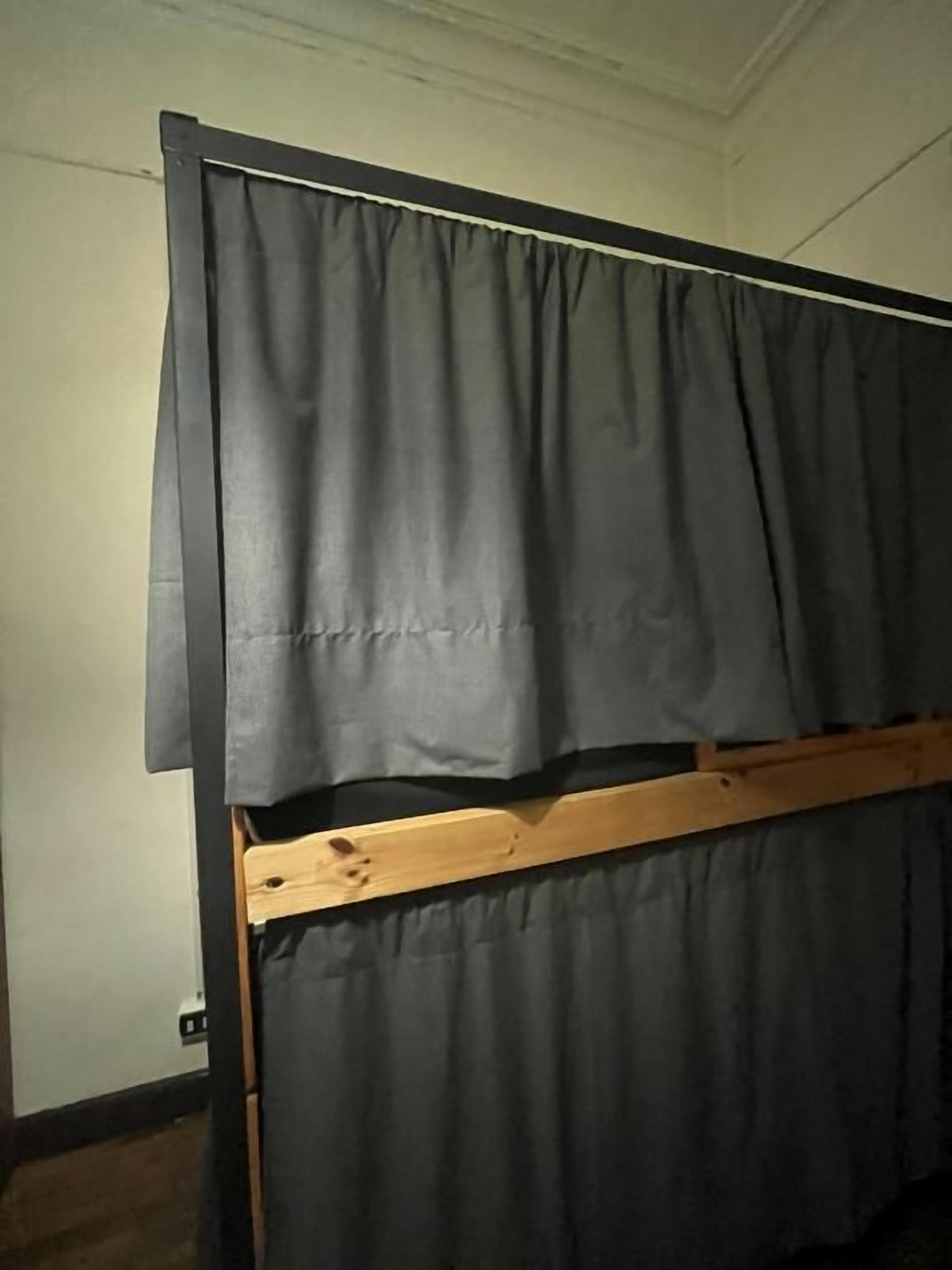Ein Zimmer mit einem Bett, das einen Holzrahmen und graue Vorhänge hat.